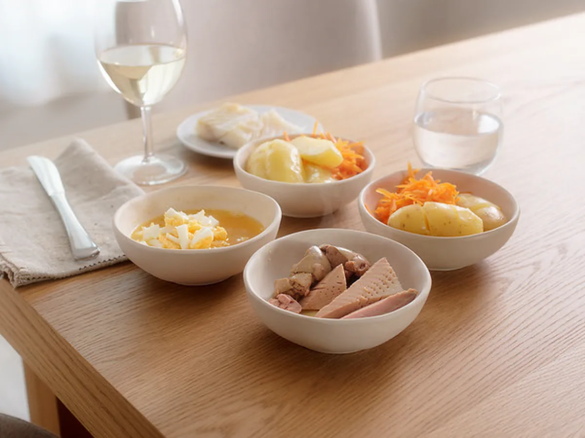 Dekket bord med eggesmør, mandelpoteter, revet gulrot, lever og rogn i skåler og et glass hvitvin